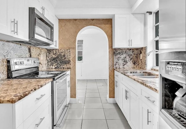 kitchen with light stone counters, light tile patterned floors, white cabinets, stainless steel appliances, and a sink