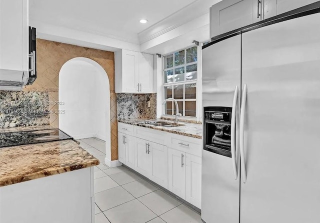 kitchen with white cabinets, stainless steel refrigerator with ice dispenser, black electric cooktop, a sink, and light stone counters