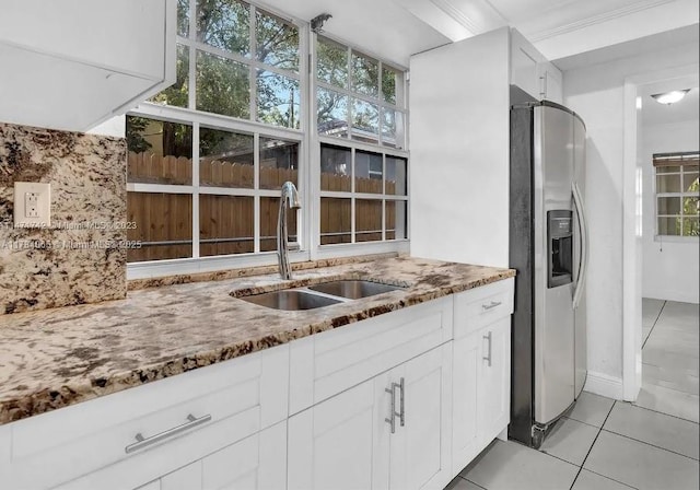 kitchen featuring light tile patterned floors, stainless steel refrigerator with ice dispenser, a sink, a wealth of natural light, and stone counters