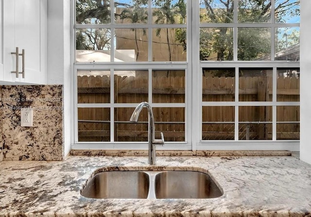 exterior details with a sink, white cabinets, and light stone counters