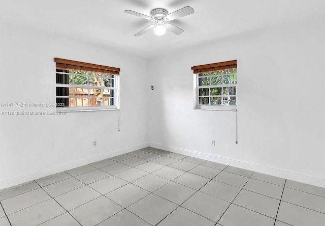 spare room with light tile patterned floors, ceiling fan, baseboards, and a healthy amount of sunlight