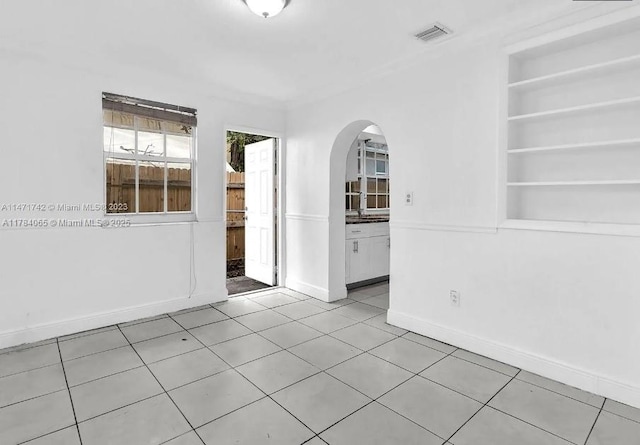 empty room featuring arched walkways, light tile patterned floors, baseboards, and visible vents