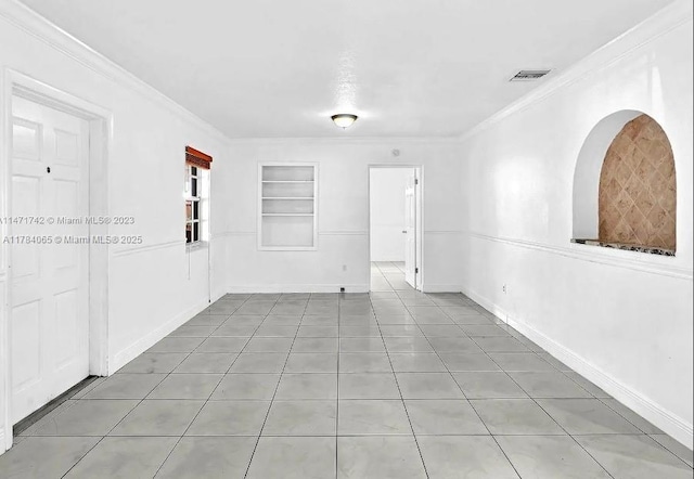 empty room with baseboards, tile patterned flooring, crown molding, visible vents, and built in shelves