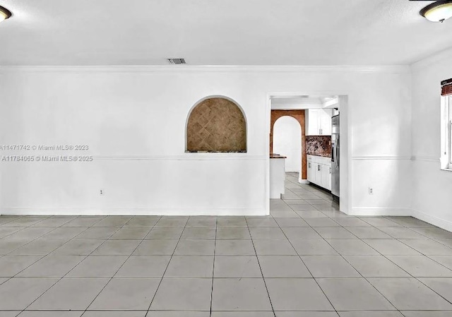 tiled empty room with baseboards, arched walkways, crown molding, and visible vents