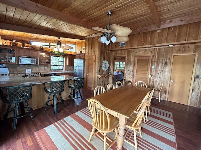 dining room with dark wood-style flooring, ceiling fan, wooden walls, and a wealth of natural light