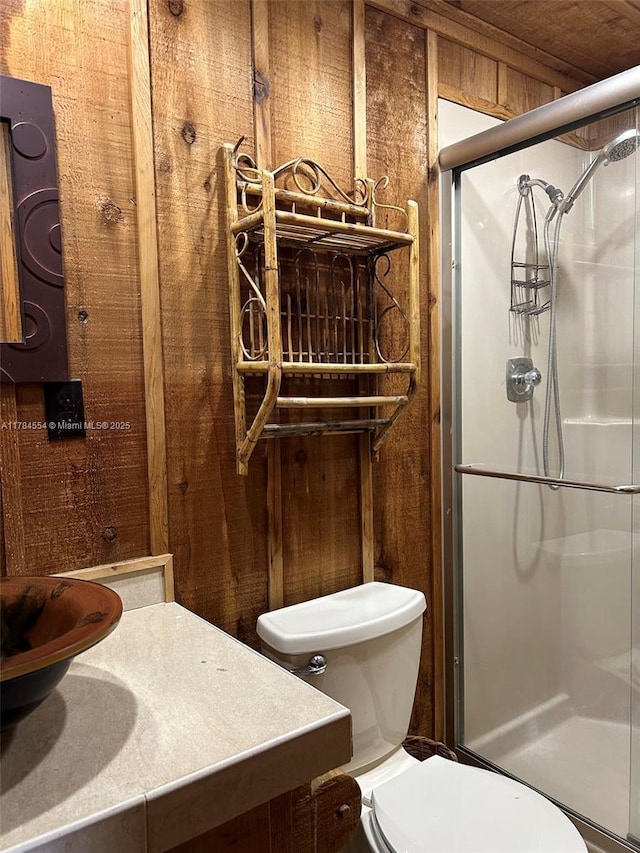 bathroom featuring vanity, a stall shower, wooden walls, and toilet