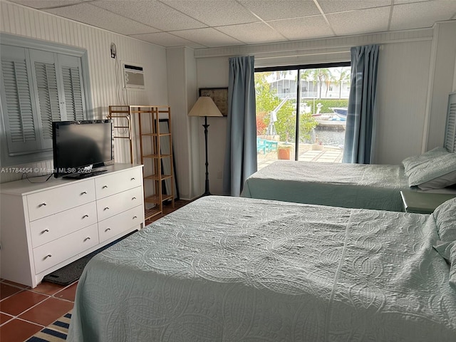 bedroom with dark tile patterned flooring, a paneled ceiling, a wall mounted air conditioner, and access to exterior