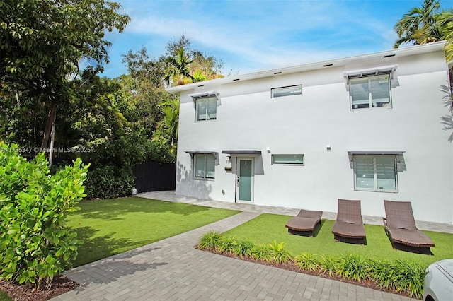 back of property with stucco siding and a lawn