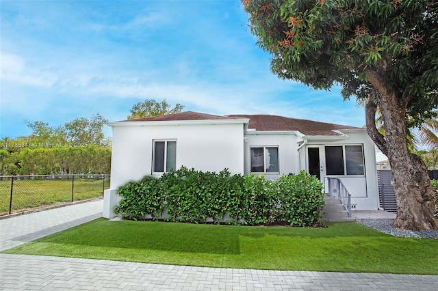 view of front of property featuring stucco siding, fence, and a front lawn