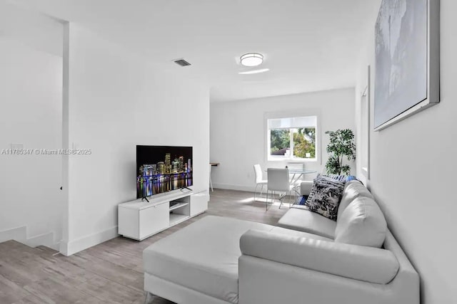 living room with light wood-type flooring, baseboards, and visible vents