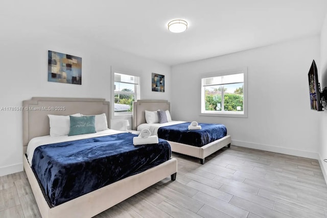bedroom with wood finished floors, baseboards, and multiple windows