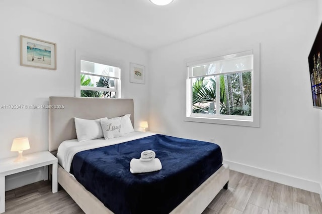bedroom with baseboards, multiple windows, and wood finished floors