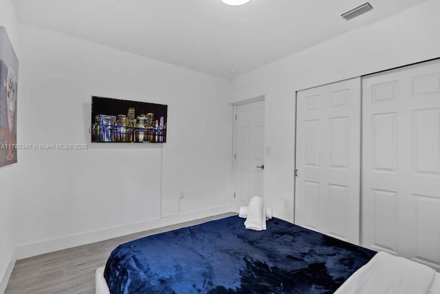 bedroom featuring a closet, visible vents, baseboards, and wood finished floors