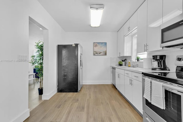 kitchen featuring a sink, light countertops, appliances with stainless steel finishes, white cabinetry, and light wood finished floors