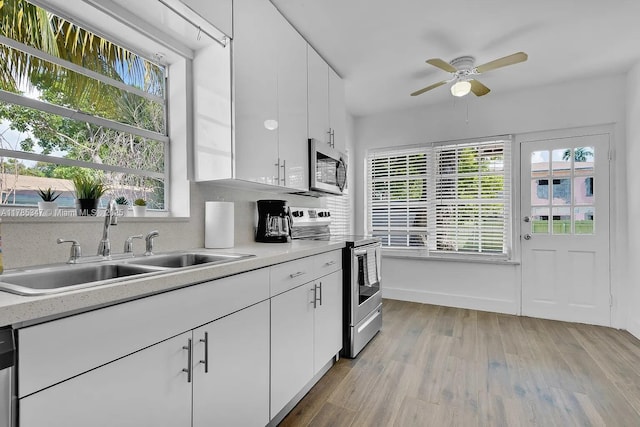 kitchen with a sink, light countertops, ceiling fan, appliances with stainless steel finishes, and light wood-type flooring