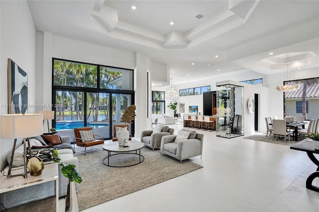 living area with recessed lighting, visible vents, a raised ceiling, a notable chandelier, and a high ceiling