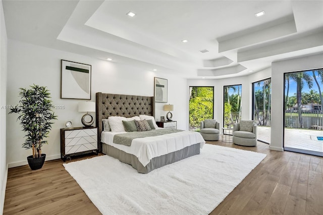 bedroom with recessed lighting, wood finished floors, access to exterior, baseboards, and a tray ceiling