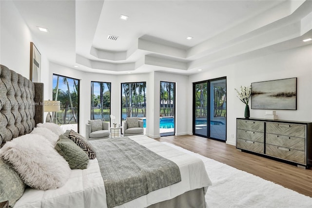 bedroom with visible vents, a tray ceiling, baseboards, wood finished floors, and access to outside