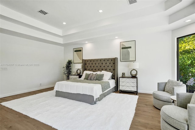 bedroom with recessed lighting, a raised ceiling, visible vents, baseboards, and wood finished floors