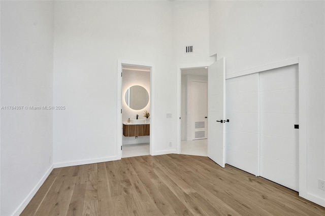 unfurnished bedroom with connected bathroom, a closet, visible vents, light wood-style flooring, and baseboards