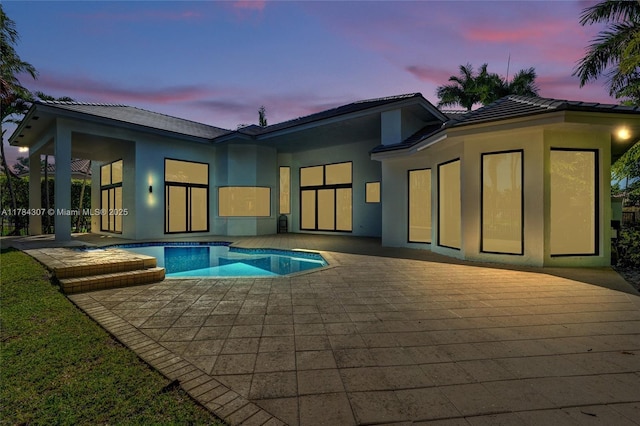back of house at dusk featuring a pool with connected hot tub, stucco siding, a tiled roof, and a patio area