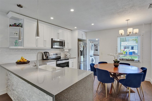 kitchen featuring stainless steel appliances, a sink, tasteful backsplash, stacked washing maching and dryer, and dark wood-type flooring
