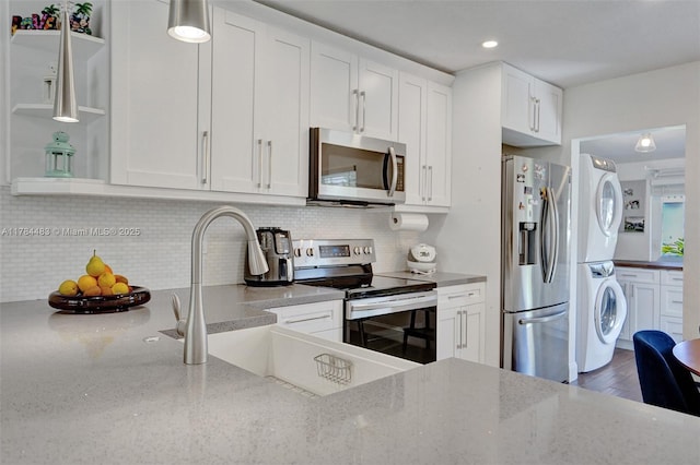 kitchen with white cabinets, stainless steel appliances, a sink, stacked washer and clothes dryer, and light stone countertops