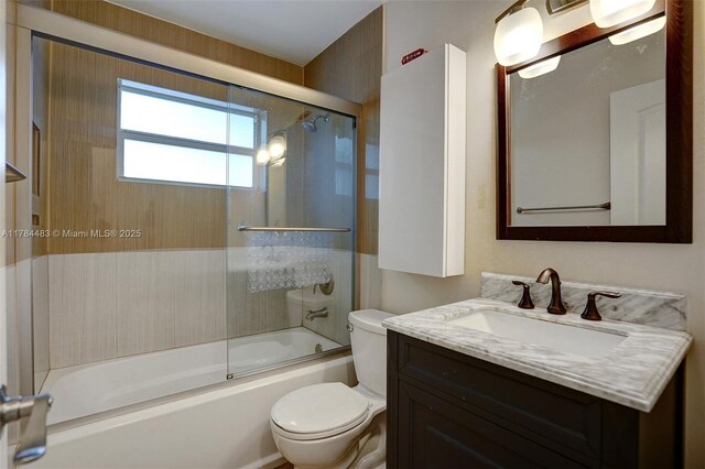 full bath featuring toilet, vanity, and shower / bath combination with glass door