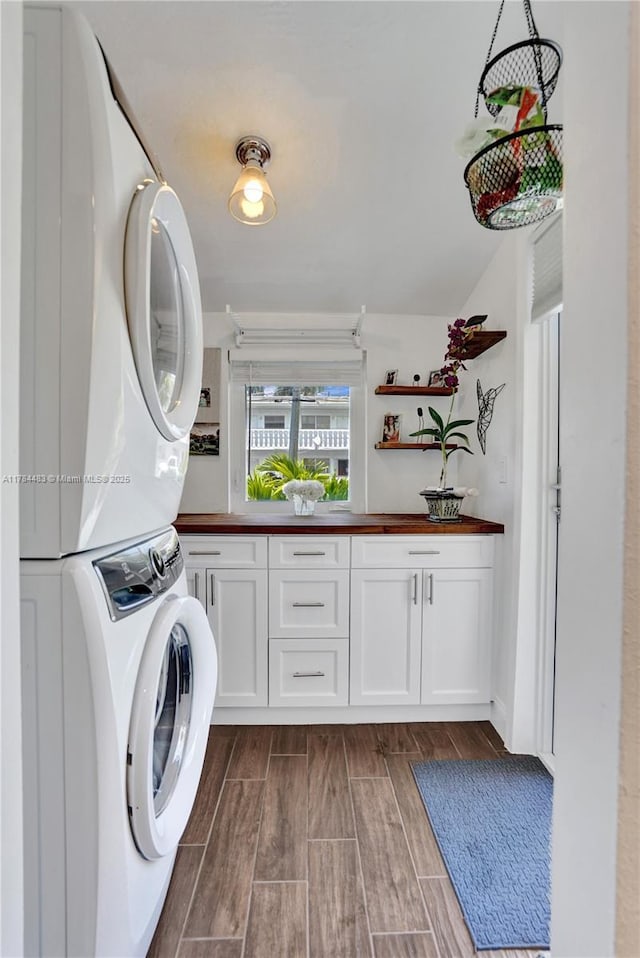 laundry area featuring stacked washer and dryer, wood finish floors, and cabinet space