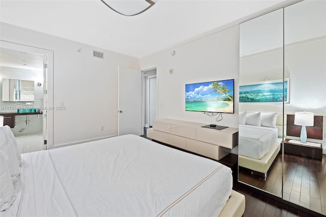 bedroom featuring dark wood-style flooring, visible vents, and ensuite bath