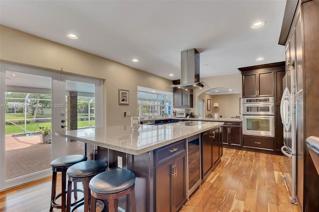 15801 SW 77th Ct, Palmetto Bay, FL 33157 - kitchen with island exhaust hood, double oven, a breakfast bar, beverage cooler, and light wood finished floors