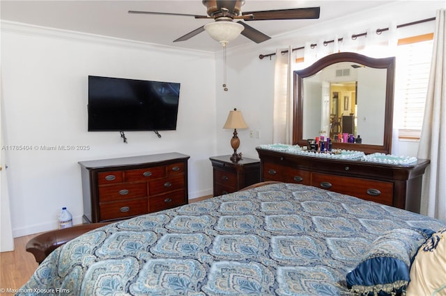 bedroom featuring a ceiling fan, ornamental molding, visible vents, wood finished floors, and baseboards
