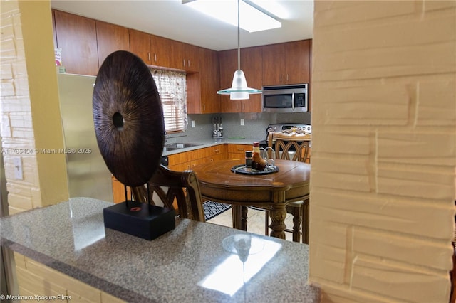 kitchen with stainless steel microwave, decorative light fixtures, brown cabinets, decorative backsplash, and electric range oven