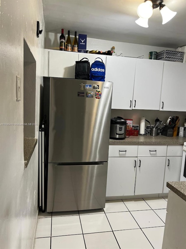 kitchen with white cabinets, light tile patterned floors, freestanding refrigerator, and dark countertops