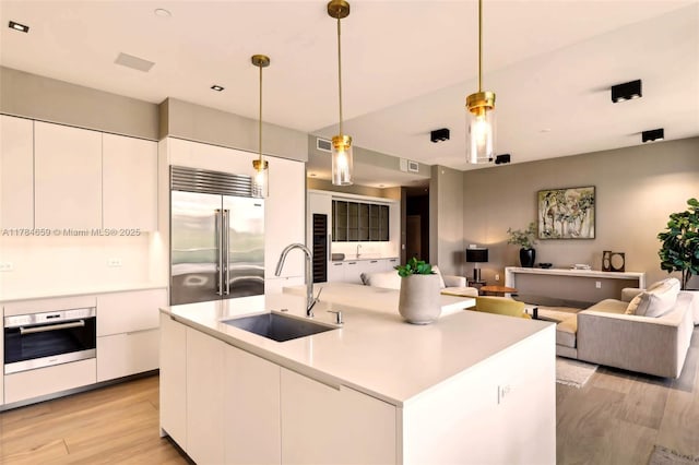 3581 E Glencoe St Unit 309, Miami, FL 33133 - kitchen with a sink, stainless steel appliances, light wood-type flooring, white cabinetry, and modern cabinets