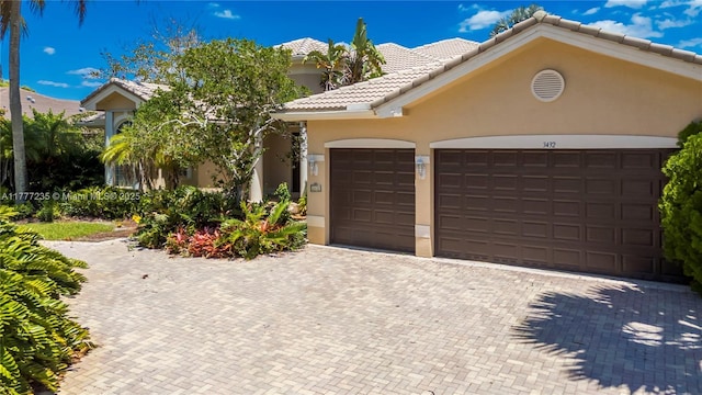 ranch-style house featuring an attached garage, a tile roof, stucco siding, and decorative driveway
