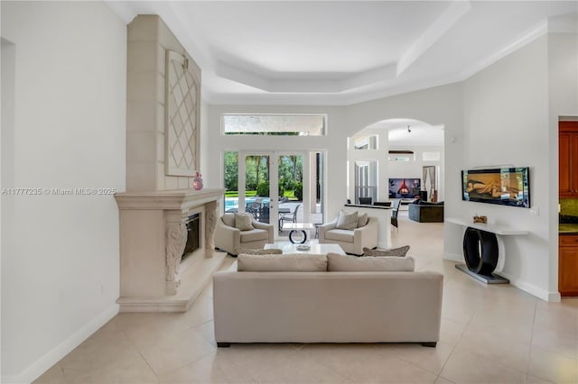 living room with a premium fireplace, light tile patterned floors, arched walkways, a towering ceiling, and a raised ceiling