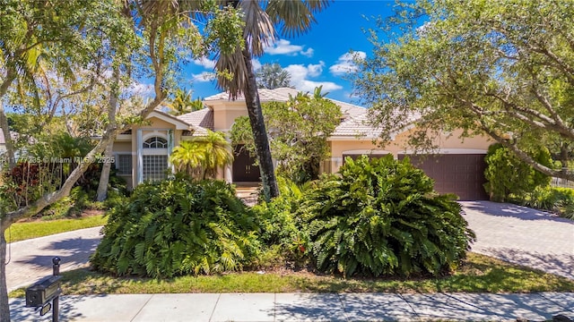 obstructed view of property with a garage, a tile roof, driveway, and stucco siding