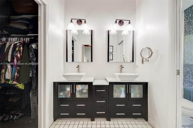 bathroom with a walk in closet, double vanity, baseboards, and a sink