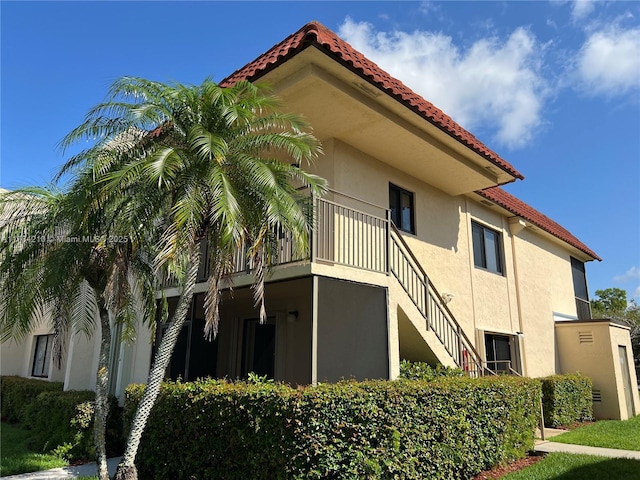 view of side of home featuring a tile roof, stairs, a balcony, and stucco siding