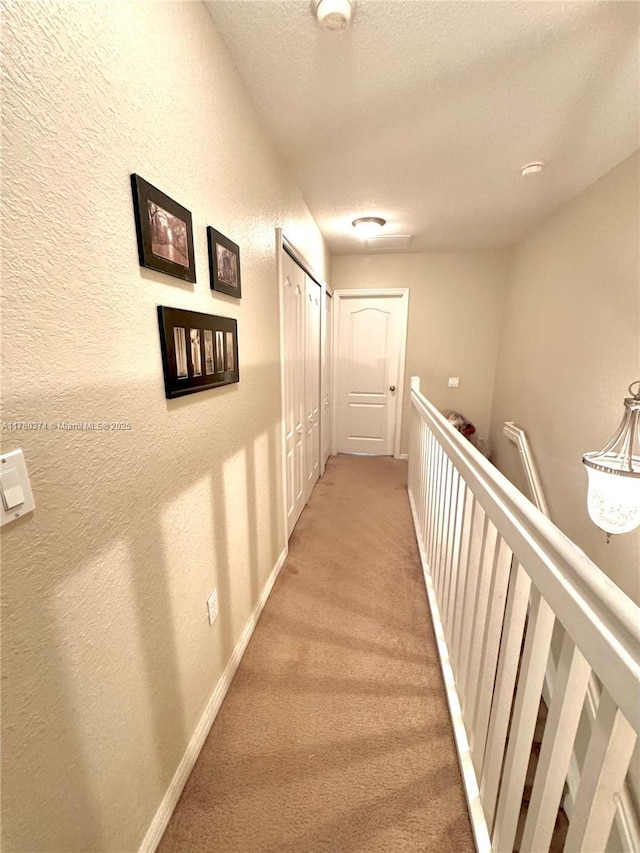 hall with a textured ceiling, carpet flooring, a textured wall, and baseboards