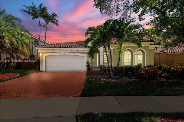 mediterranean / spanish-style house featuring decorative driveway, stucco siding, an attached garage, and a tiled roof