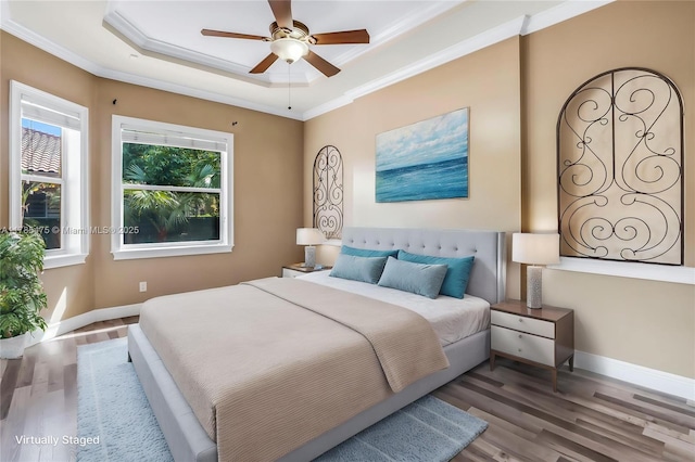 bedroom featuring wood finished floors, ornamental molding, a tray ceiling, and baseboards