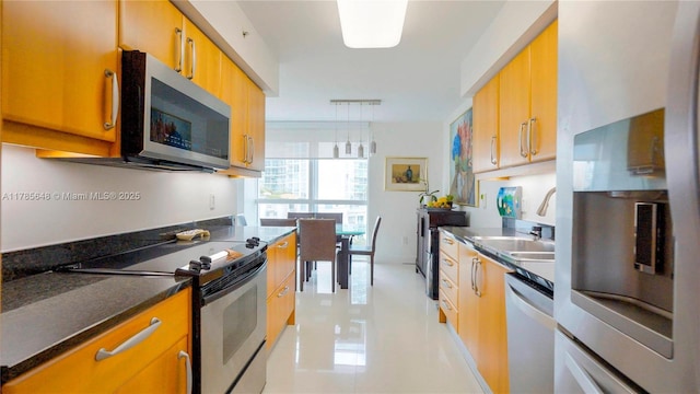 kitchen with stainless steel appliances, brown cabinetry, a sink, light tile patterned floors, and hanging light fixtures