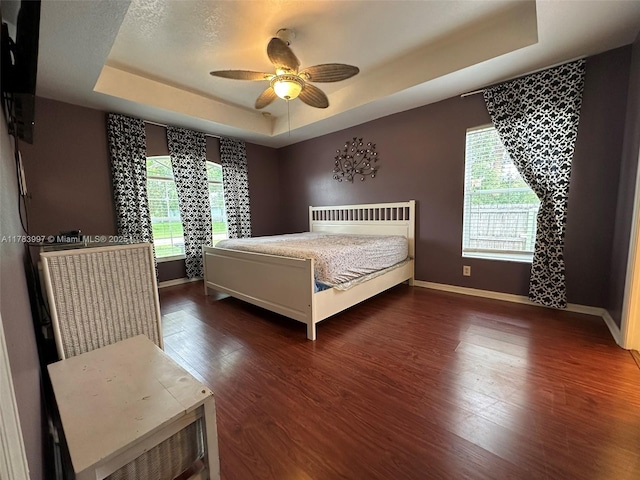 1214 SW Patricia Ave, Port St Lucie, FL 34953 - bedroom featuring a tray ceiling, baseboards, wood finished floors, and a ceiling fan