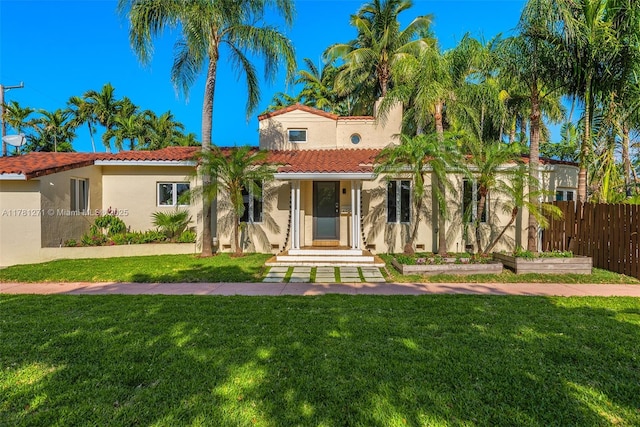 mediterranean / spanish-style home featuring a tiled roof, a front lawn, fence, and stucco siding