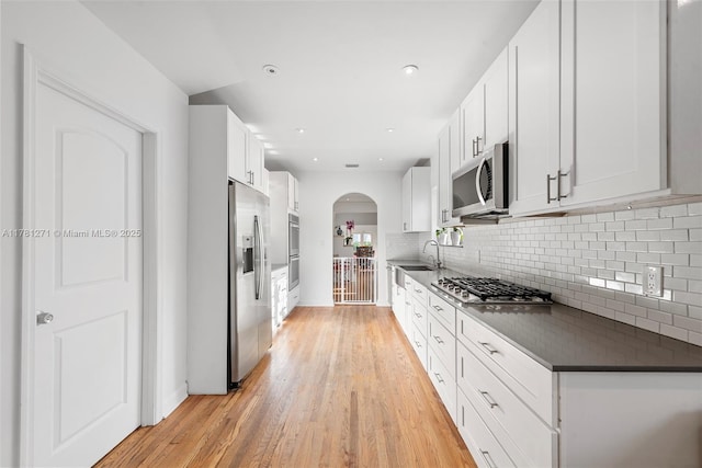 kitchen featuring light wood-type flooring, backsplash, dark countertops, stainless steel appliances, and arched walkways