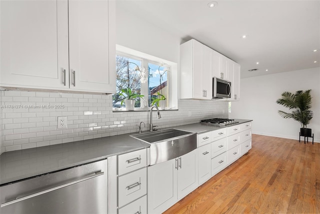 kitchen with light wood-style flooring, white cabinetry, backsplash, stainless steel appliances, and a sink