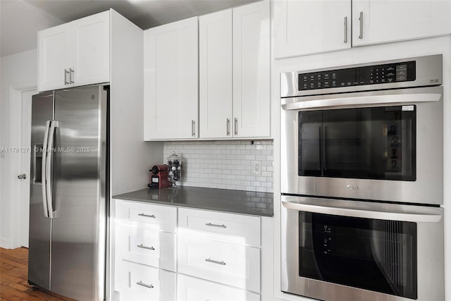 kitchen with backsplash, dark countertops, white cabinets, dark wood finished floors, and stainless steel appliances