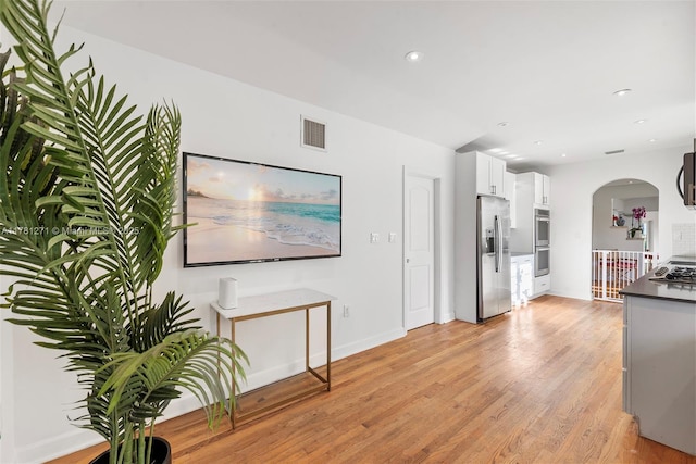 kitchen with light wood-type flooring, arched walkways, white cabinetry, visible vents, and appliances with stainless steel finishes